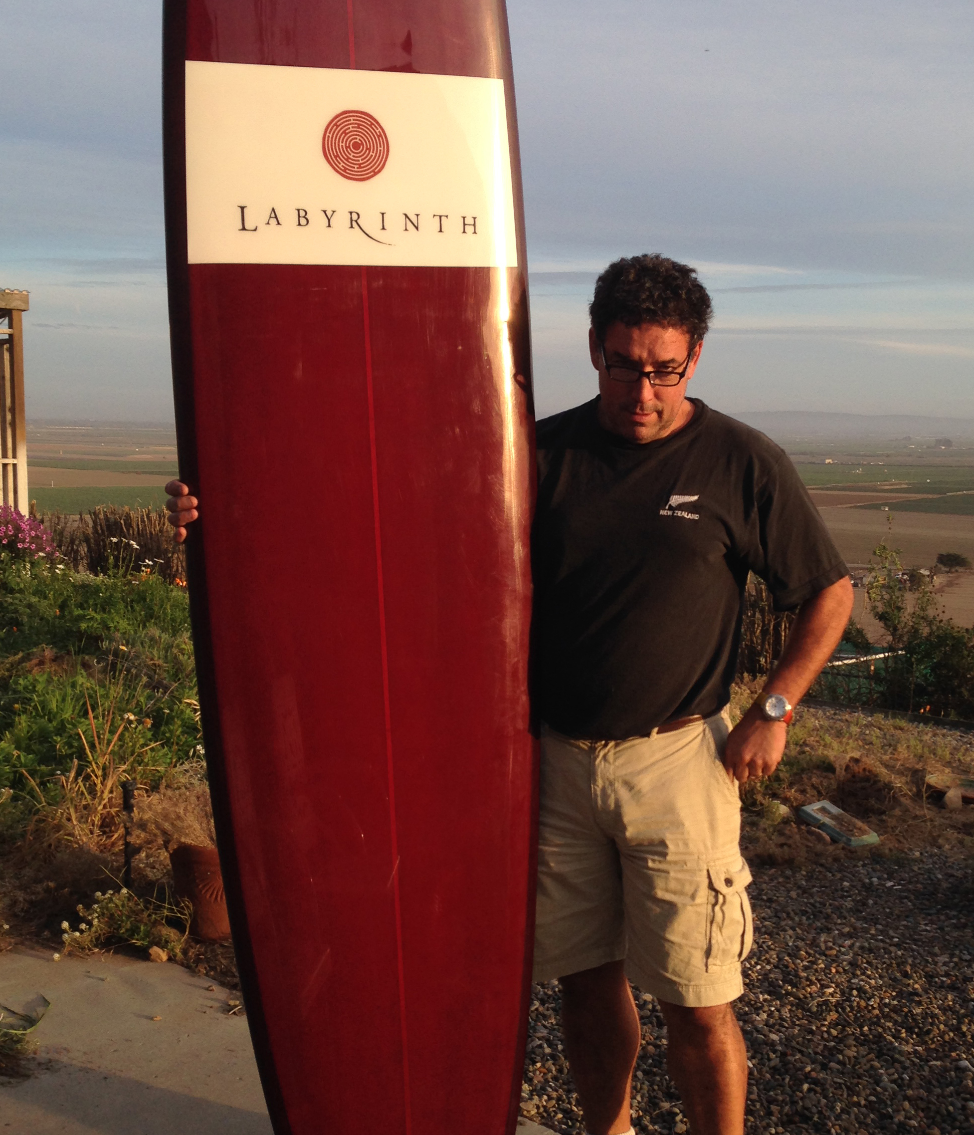 Rick Hill of Labyrinth next to surfboard with Labyrinth logo