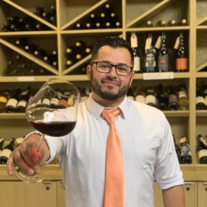 Wine Director Jon Lynn Holding a glass of red wine in front of wine wall